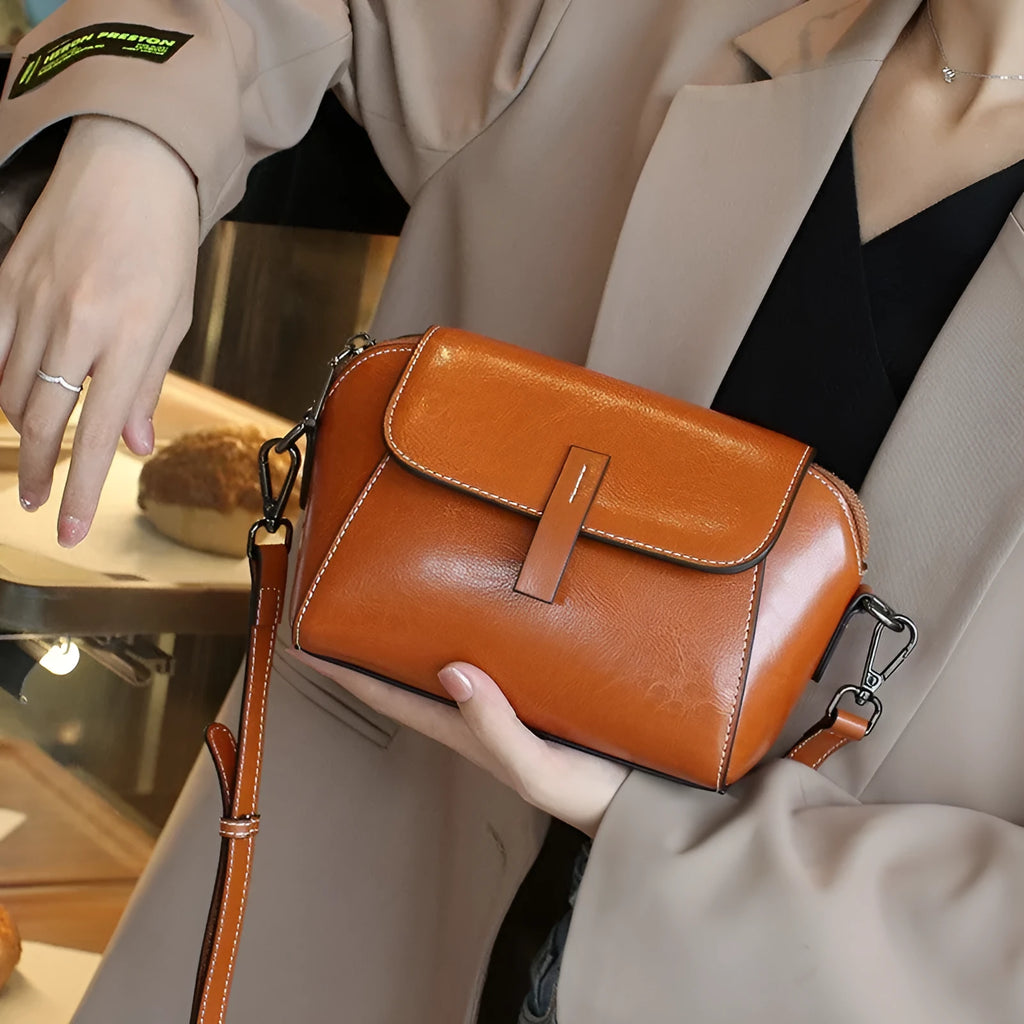 Brown women's shell-shaped genuine leather messenger bag with a single cross-body strap and visible stitching.