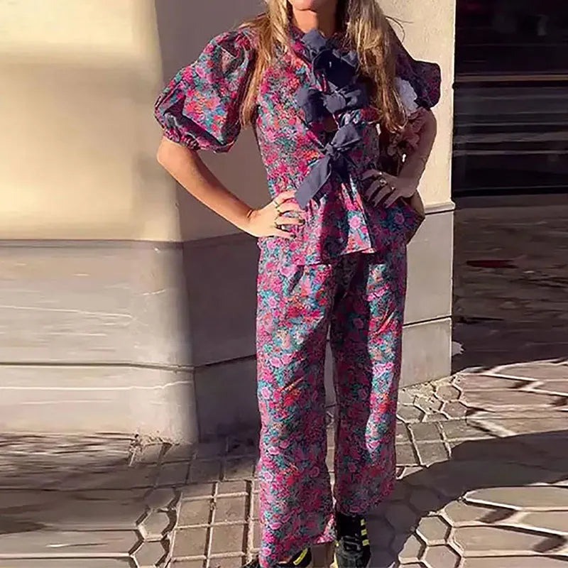 Women's floral print two-piece suit with a tie-neck puff sleeve blouse and straight-leg trousers.