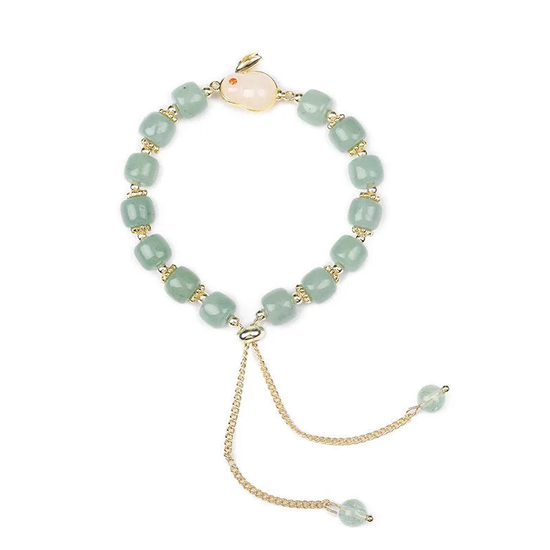 Rabbit charm bracelet with green aventurine or strawberry quartz stones and gold accents on a wrist.