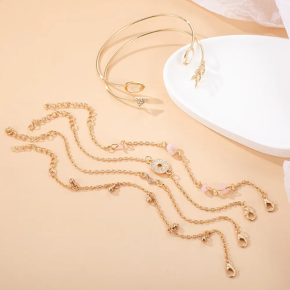 Set of six gold bracelets with arrow, V-shape, and water droplet charms on a dark background.