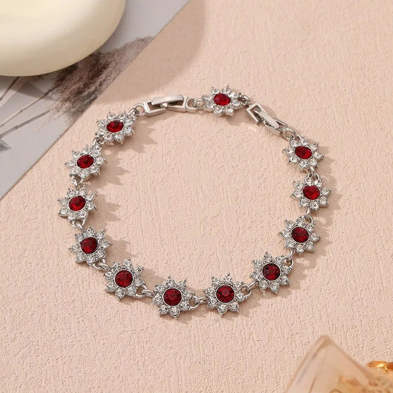 Floral shaped zinc alloy bracelet with electroplated silver finish and red coloured gemstones.