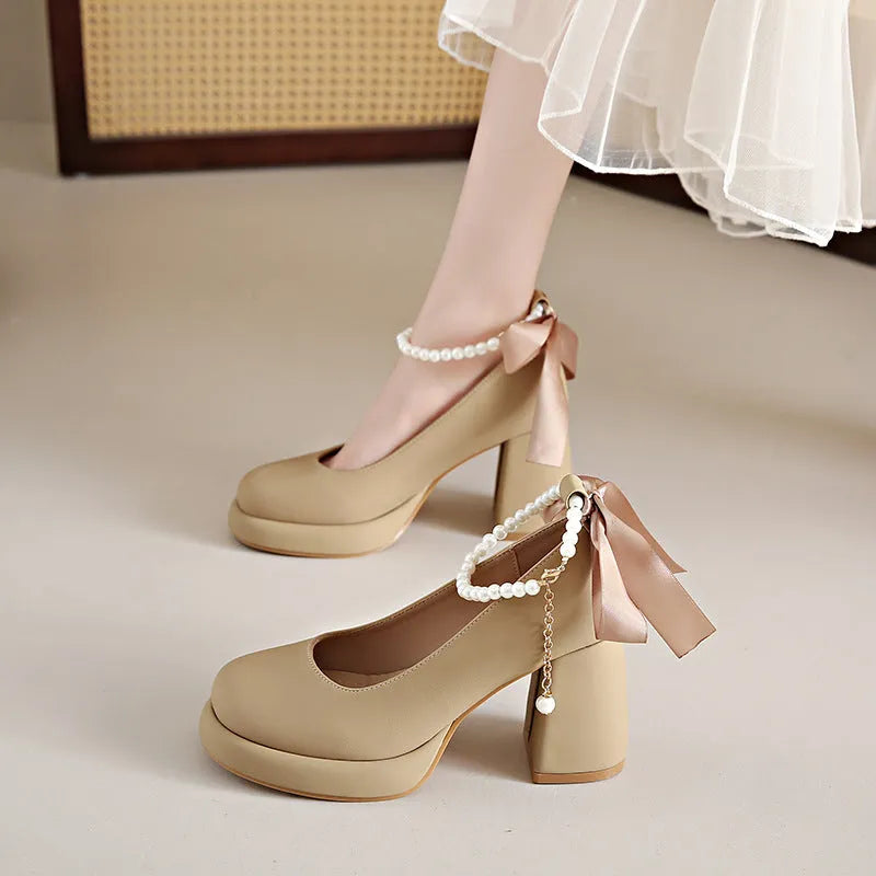 Beige women's Mary Jane shoes with a chunky block heel, ankle strap buckle, and round toe with pearl detail.