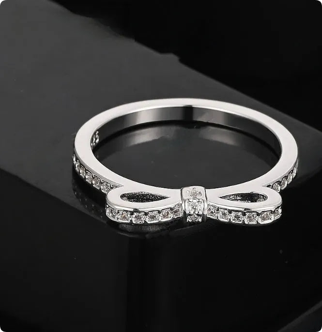 A silver-coloured bow-shaped ring set with sparkling clear rhinestone crystals on a finger.