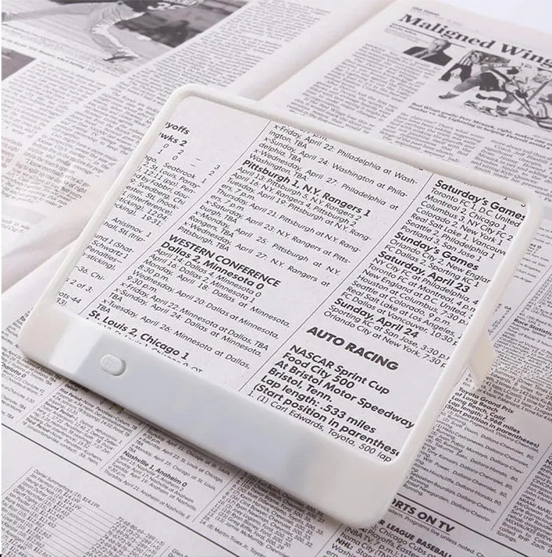 Black and white LED magnifying glass with 3x lens on a desktop next to a book.