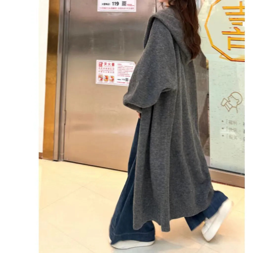 A woman wearing a long, hooded, beige knitted cardigan in a relaxed Korean style.