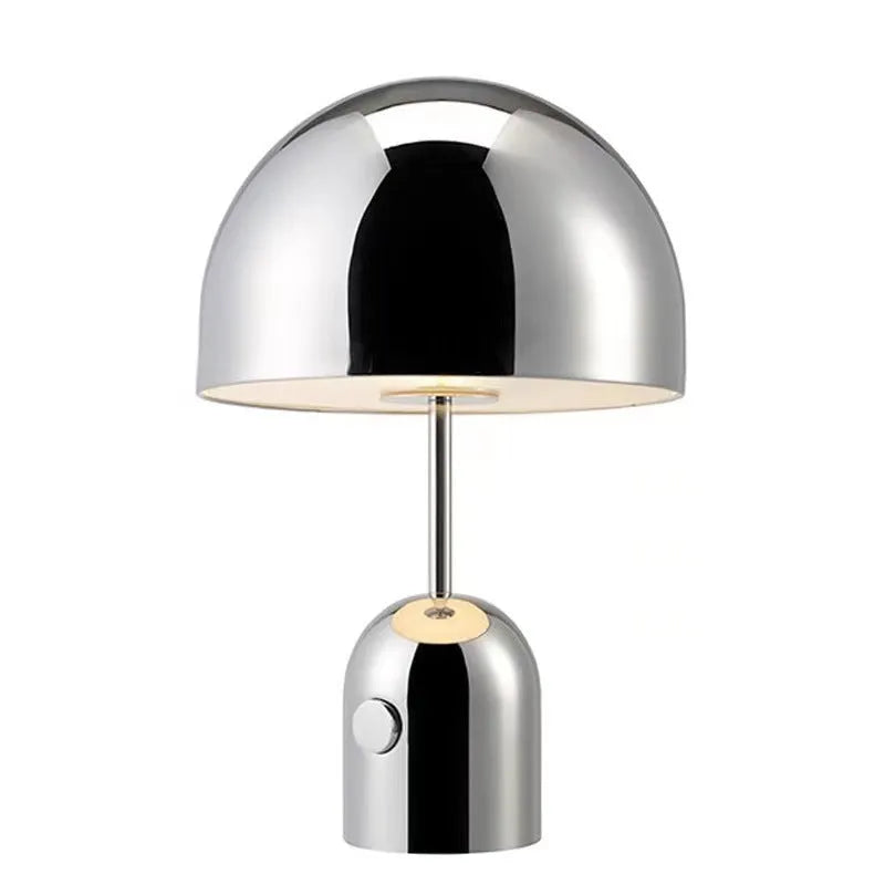 Modern mushroom cap table lamp with a metal base in rose gold finish on a wooden table.