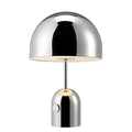 Modern mushroom cap table lamp with a metal base in rose gold finish on a wooden table.