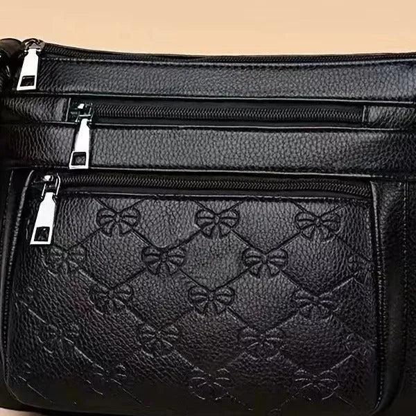 Black women's crossbody bag with butterfly embossed pattern and adjustable shoulder strap.