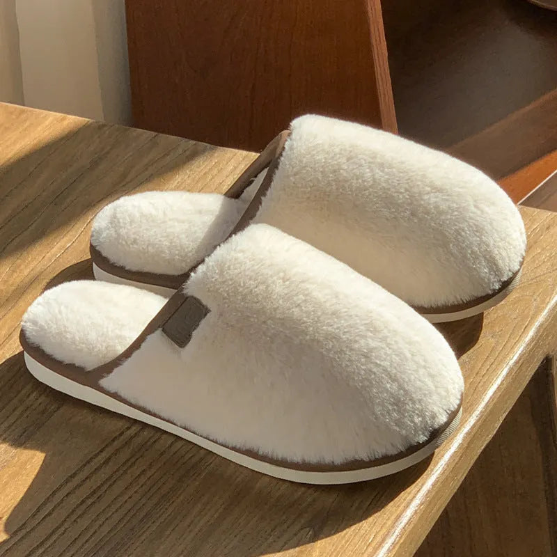 Pair of solid blue plush winter slippers with non-slip PVC sole on a wooden floor.