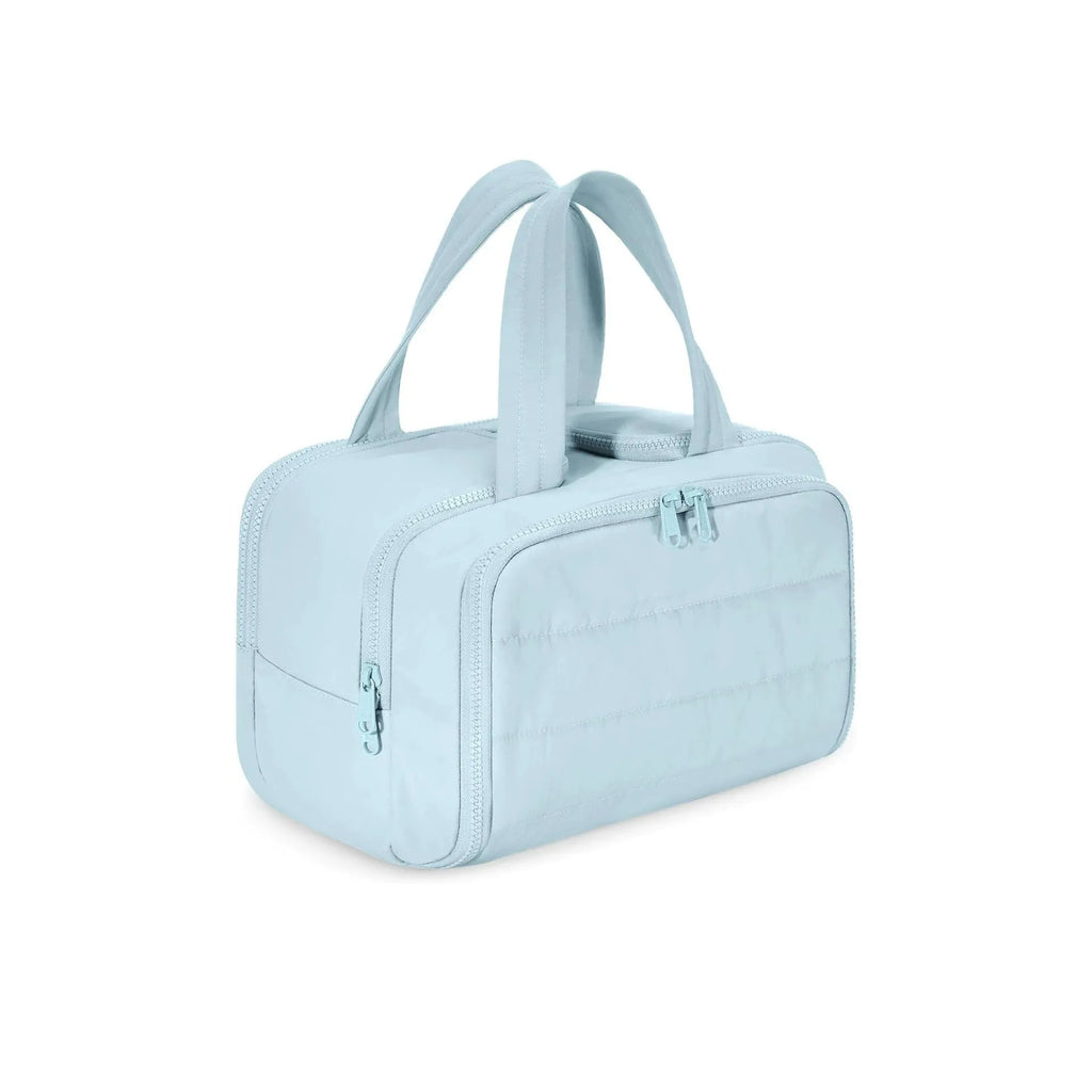 Large beige travel toiletry bag with wide open top, shown next to cosmetic bottles.