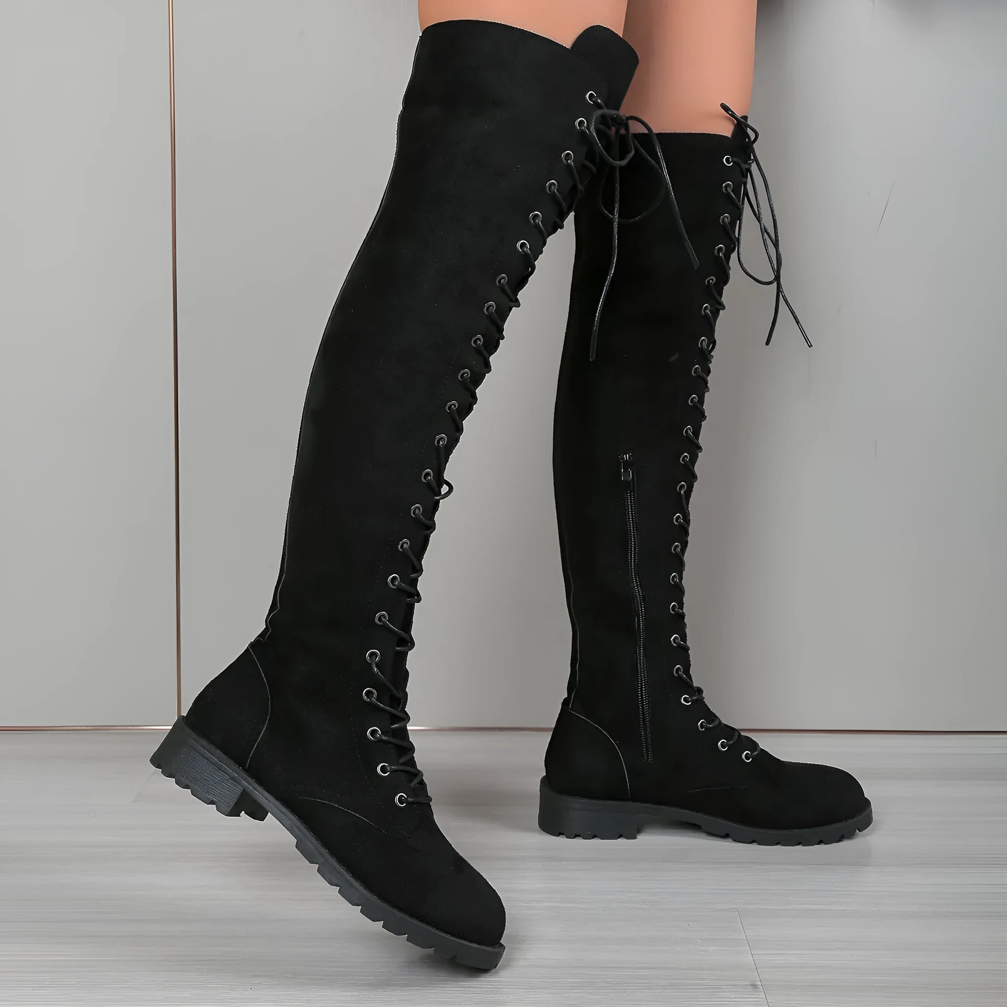 Black lace-up over-the-knee flat boots with round toe and stitching detail on a neutral background.