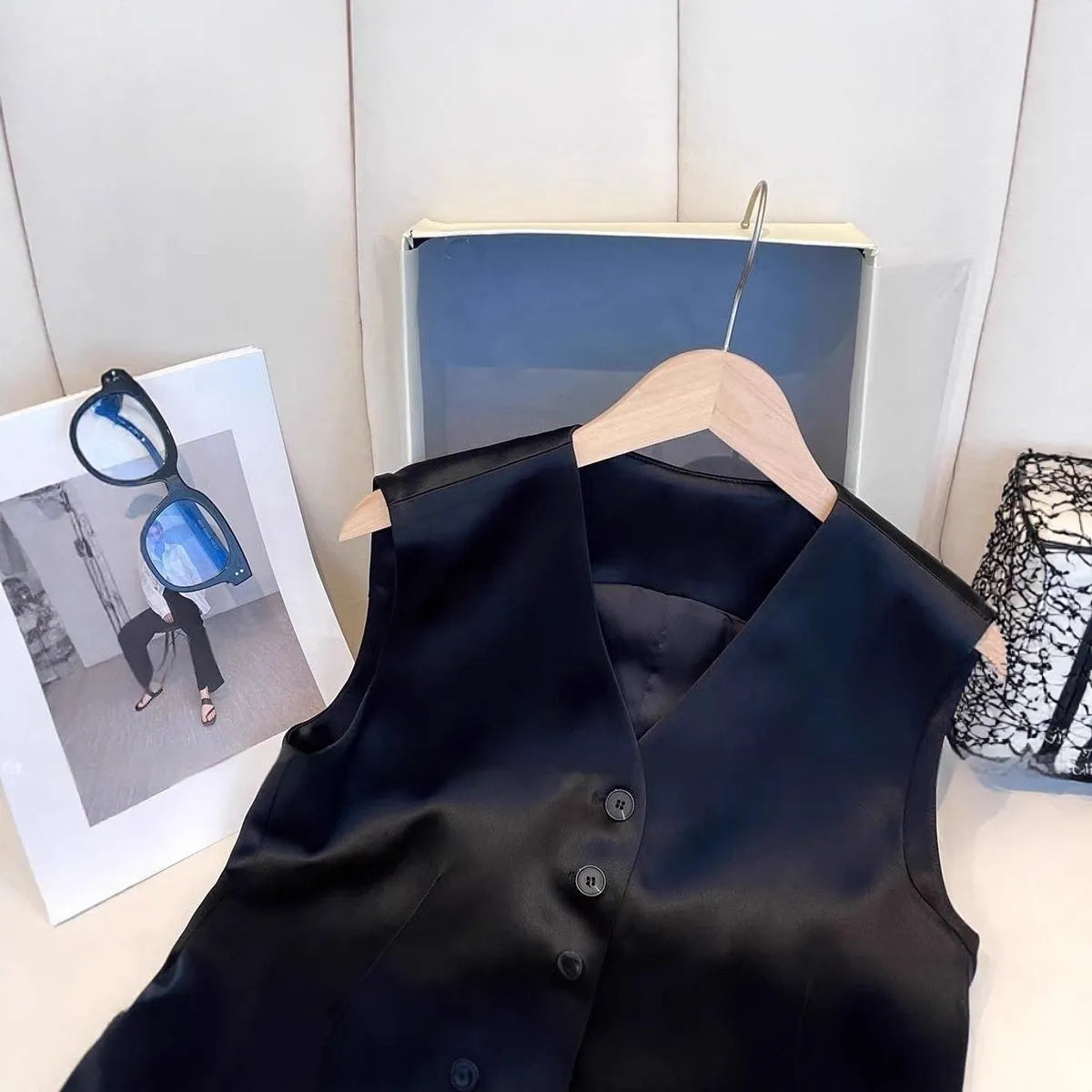 Black satin sleeveless vest for women on a hanger, showing loose fit and splicing detail