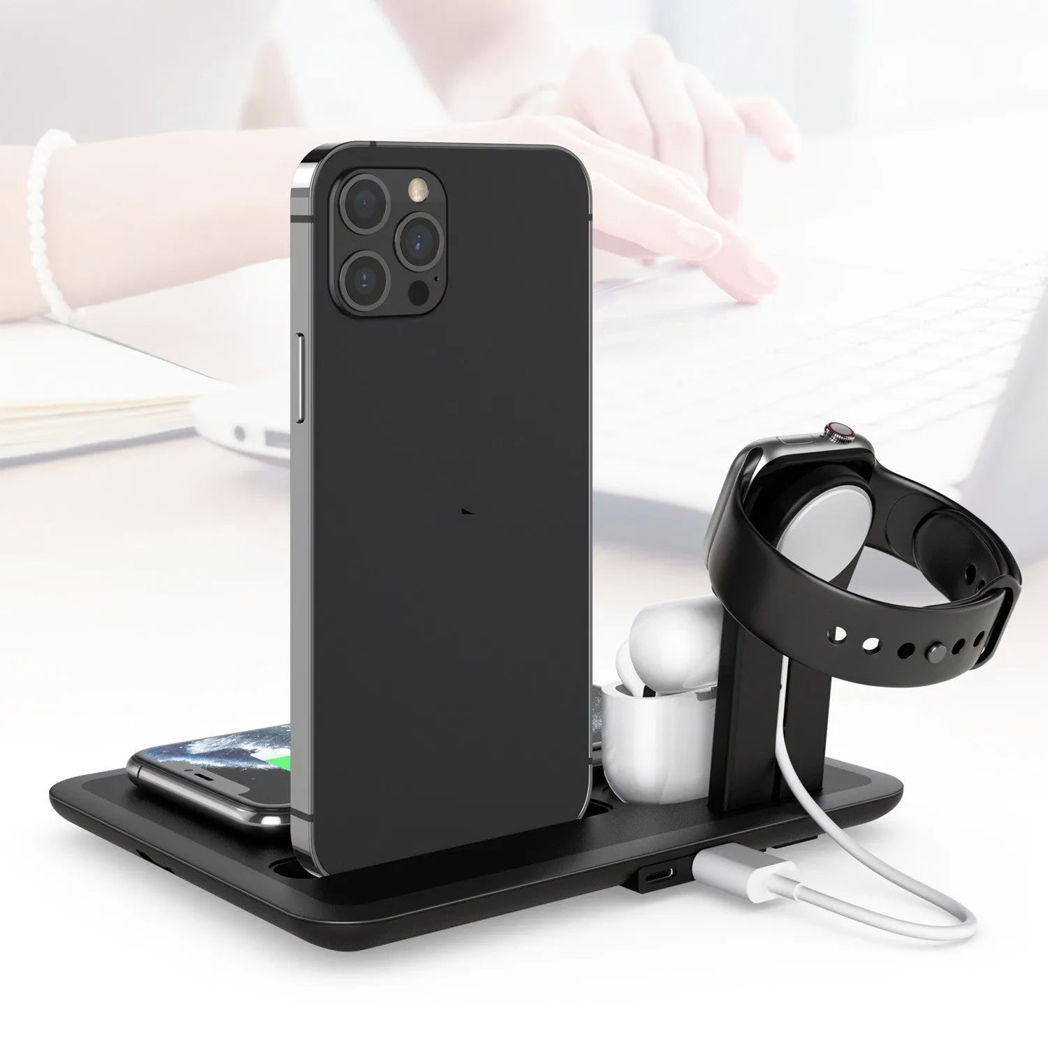 Black wireless charging desk bracket with phone on Qi pad, watch and headphones connected to wired charging ports