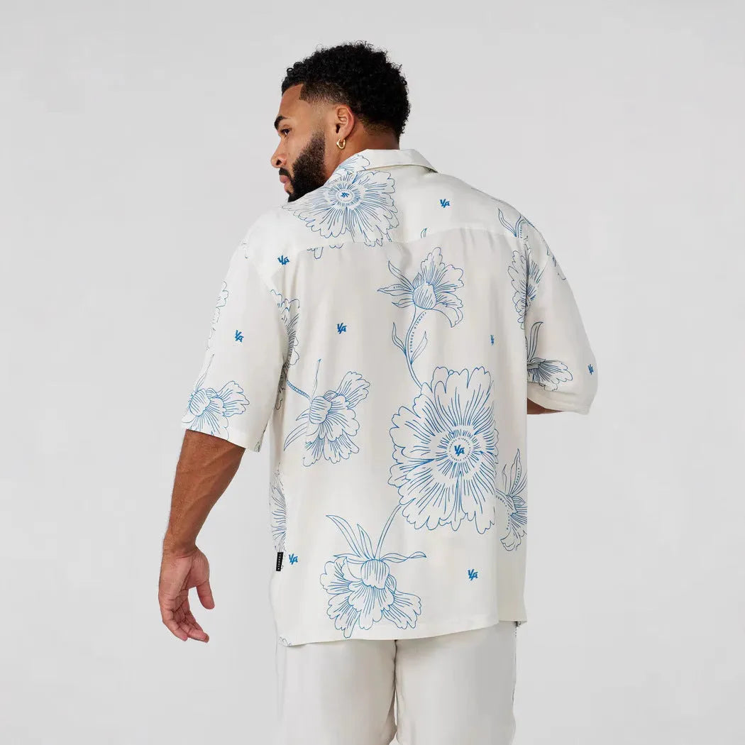A man's loose-fit short sleeve printed top with a floral pattern, shown in a light colour on a hanger.