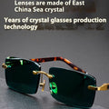 A pair of frameless sunglasses with dark green crystal lenses, shown with a glasses case and cleaning cloth.