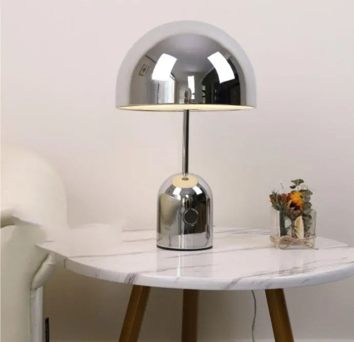Modern mushroom cap table lamp with a metal base in rose gold finish on a wooden table.