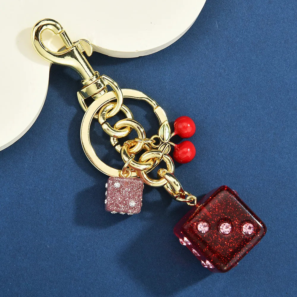 Close-up of a square metal keychain pendant with a two-tone red cherry dice pattern.
