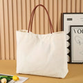 Beige white canvas tote bag with a front zip pocket and sturdy shoulder straps laid flat.